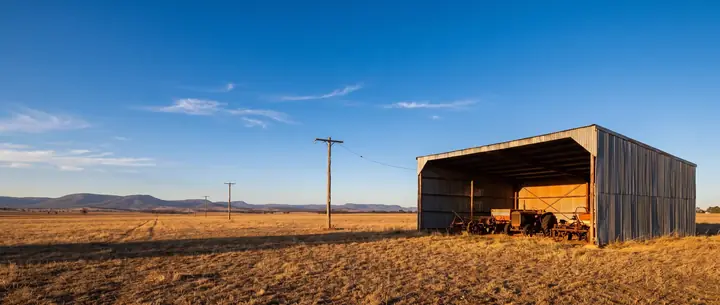 Farm machinery shed with power poles running across a paddock